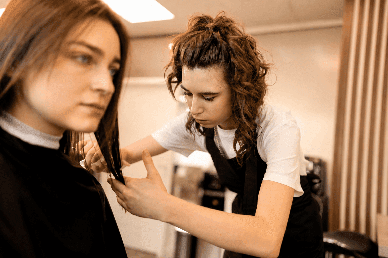 Hairdresser precisely cutting a young woman's long brown hair in a modern salon.